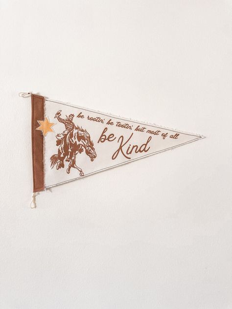 Add a dose of cowboy in your home with the "Rootin', Tootin', Be Kind" Pennant. A sheriff's star patch is added to give your flag a unique and dimensional look. Two layers of canvas fabric are sewn together for a durable, high quality feel. Display on wall easily with twine loops.  -Measures 10 x 18 inches Flag Pennant Banner, Framed Pennant Flag, Cowboy Themed Nursery, Name Pennant, Word Art Wall, Rootin Tootin, Cowboy Decor, Pennant Flags, College Room