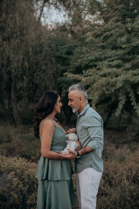 A couple stands in a forest, lovingly holding their newborn between them, with both parents gazing at each other, encapsulating a moment of family bliss in nature. Family In Nature, Family Outdoor Photoshoot, Newborn Photoshoot Ideas, Coordinated Outfits, Newborn Birth, Couple Dress, Birth Photography, Outdoor Photoshoot, Photography Pricing