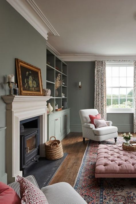 A formal drawing room for entertaining and relaxing. Pink and red fabrics compliment the green walls. An ottoman displayed in the centre in front of a wood burning stove, with arm chairs and built in wooden cabinetry. Cosy Living Room Colours, Classic Drawing Room, Formal Drawing Room, Red Velvet Sofa, Classic Drawing, Deep Red Velvet, Drawing Room Interior, Drawing Room Interior Design, Interior Design Work