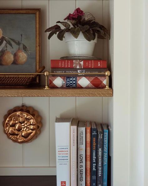 This joyous bookshelf nestled off of the #PartridgePlace kitchen serves as an extra storage space for kitchen essentials and stands as a reminder to never shy away from the details + appreciate every corner of your home. 😊 From the sconce lighting to the intricate brass gallery rail and beadboard accents, every element was carefully chosen to create a warm welcome to the kitchen from the foyer in this curated niche. ✨ . . . . . #spotthenewtrend #purposeinstyle #maketimefordesign #ighomes #mys... Styling Kitchen Bookshelves, Kitchen Shelves For Cookbooks, Recipe Book Shelf Kitchen, Cookbook Collection Display, How To Display Cookbooks In Kitchen Open Shelves, Cookbooks In Pantry, Cookbook Storage Small Kitchen, Kitchen Cook Book Shelf, Cook Book Storage Ideas Kitchens