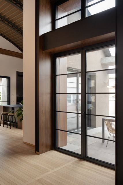 Finestre a tutta altezza con telaio nero, incorniciate da dettagli in legno, che si affacciano su una terrazza esterna. L'interno presenta un pavimento in legno chiaro e un design moderno e raffinato. Design Minimalista, Loft, Interior Design, Design