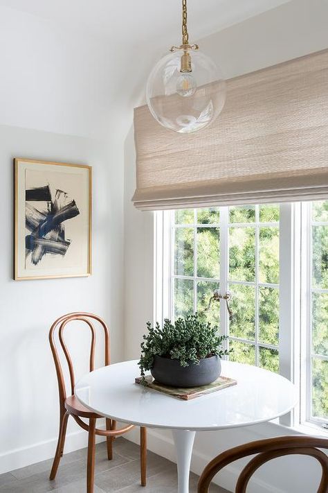 A Katie Globe Pendant lights a Saarinen dining table seating two bentwood dining chairs in front of a window covered in a linen roman shade. Light Grey Wood Floors, Saarinen Dining Table, Linen Roman Shades, Saarinen Table, Woven Dining Chairs, Linen Dining Chairs, Dining Table Gold, Transitional Dining Room, Dining Table Lighting