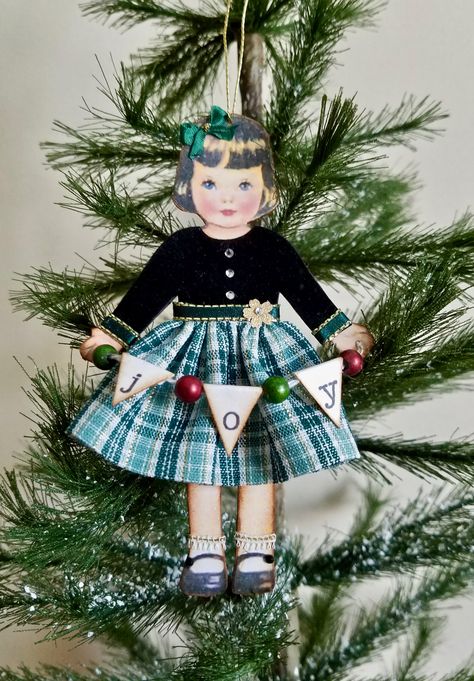 Handmade paper doll ornament wearing a green plaid holiday dress and holding a JOY paper garland.  For sale in my etsy shop NeedleandThreadLLC. Dresden Houses, Christmas Paper Dolls, Paper Doll Craft, Doll Ornaments, Cozy Christmas Decor, Christmas Card Crafts, Vintage Paper Dolls, Paper Garland, Christmas Ornaments Homemade