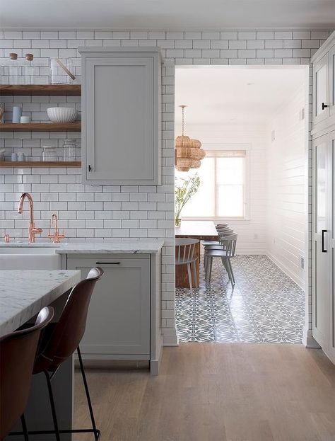 Light gray kitchen accented with gray wash wood floors boasts light gray shaker cabinets donning oil rubbed bronze hardware and a white marble countertop holding a farmhouse sink with a copper gooseneck faucet beneath stacked wooden shelves flanked by gray upper cabinets mounted on a white subway tile backsplash contrasted with dark grout. Gray Wood Tile Flooring, Light Grey Kitchens, Серая Кухня, Wood Floor Kitchen, Terrazzo Tile, Amazing Kitchen, Kitchen Transformation, Kitchen White, White Marble Countertops