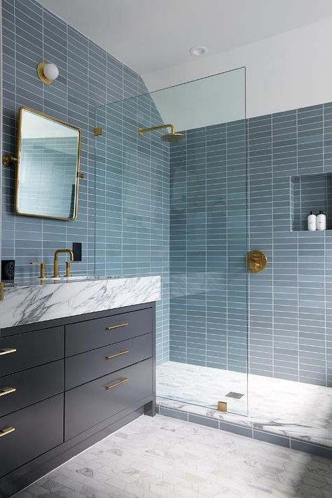 Bathroom features shower with stacked blue glass tiles, a blue tiled shower niche, aged brass shower kit, gray marble hexagon floor tiles and a glass partition next to a dark blue washstand topped in marble under a rectangular pivot mirror. Blue Shower Tile, Blue Glass Tile, Blue Bathroom Tile, Marble Bathtub, Shower Fixtures, Blue Tile, Shower Niche, Blue Bathroom, Blue Tiles