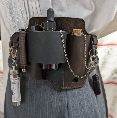 Leather belt sheath with pockets and rings to hold vials, bottles, and tools. All included accessories have chains and clasps which are available in bronze or silver. Included: - Leather belt sheath with center pass through loop on back for stability.  For pockets with no bottom support, I've added chains and clasps so bottles and vials can attach to a ring or hook. - 1 large (4") amber glass dropper bottle - 2 aluminum vials with screw tops(with rubber gaskets) - one black, one silver.  These v Utility Belt Aesthetic, Medieval Utility Belt, Fantasy Belt Pouch, Alchemist Accessories, Alchemy Belt, Ren Faire Witch, Ren Faire Accessories, Witch Belt, Rogue Accessories