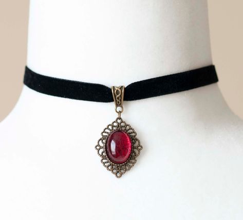 Indulge in the dark elegance of the Victorian era with this enchanting choker, crafted from luxurious black velvet ribbon and adorned with an antique bronze filigree pendant housing a blood-red glass cabochon. Perfect for enhancing your Gothic vampire aesthetic, this necklace is a timeless accessory. Key Features: Material: Black velvet ribbon and antique bronze filigree pendant with blood-red glass cabochon Choker Length: 12 inches (30.5cm), 0.4 inches (10mm) wide Pendant Size: Approximately 1 Gothic Vampire Aesthetic, Chain Rosary, Vampire Necklace, Vampire Jewelry, Black Vampire, Halloween Circus, Red Choker, Vampire Clothes, Black Velvet Ribbon