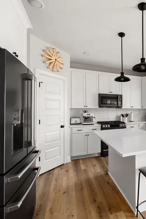 This stunning kitchen features a timeless design with white cabinets, dark stainless steel appliances, and sleek white quartz countertops. The light hardwood floors add warmth and brightness to the space. This is a beautiful example of a kitchen that is both stylish and functional. #whitekitchen #darkaccents #quartzcountertops #lightwoodfloors #timelessdesign #kitcheninspiration #interiordesign #homedecor #dreamkitchen #kitchendesign #homerenovation #kitchenmakeover #modernkitchen #luxurykitche Black Kitchen With White Appliances, White Cabinets With Black Appliances, White Appliances In Kitchen Ideas, White Kitchen With Black Appliances, White Cabinets With Black Hardware, White Cabinets Black Appliances, Black Stainless Appliances, White Quartz Countertops, White Kitchen Appliances