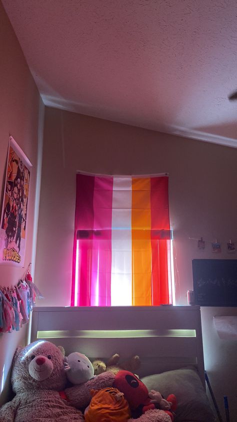 Lesbian flag over a window above a bed with stuffed animals and posters on the wall. Lesbian Flag Bedroom, Lesbian Flag Decor, Room With Lesbian Flag, Pride Flag In Bedroom, Lesbian Bedroom Ideas Aesthetic, Lesbian Flag Room, Lesbian Room Ideas, Lgbtq Bedroom, Pride Flag Bedroom