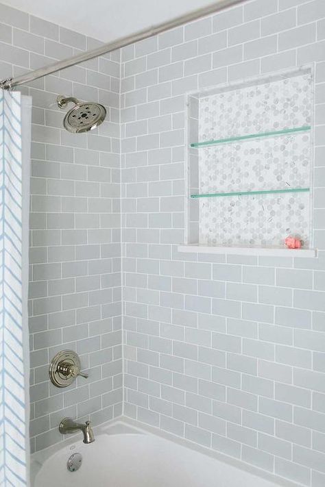 Lovely bathroom features a drop-in tub with shower accented with gray subway tile surround fitted with a marble hex tiled niche lined with glass shelves finished with a white and blue shower curtain. Gray Shower Tile, Subway Tile Showers, Grey Subway Tiles, Bad Inspiration, Bath Tiles, Transitional Bathroom, Hall Bathroom, Shower Niche, Bathroom Tub