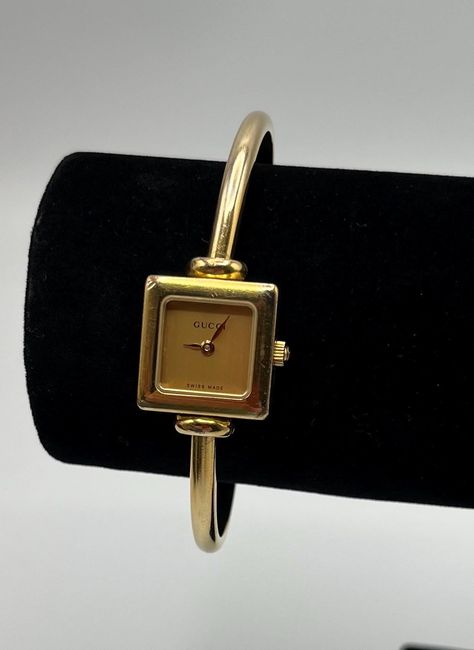 Stunning vintage ladies Gucci cocktail bangle WATCH with champagne dial detail.  This piece dates back to the late 1990s-early 2000s, and features an intriguing 20mm stainless steel case with 10 micron 18k yellow gold plated finish.  The integrated bangle-inspired bracelet is easily recognised as a signature Gucci design. Guaranteed original!  The gold tone dial and gold tone hands keep the watch face minimalist and easy to read. The crown is original and bears Gucci logo. Powering this watch is Gucci Vintage Watch, Early 2000s Jewelry, Gucci Bangle, Gucci Aesthetic, Gold Bangle Watch, 2000s Jewelry, Gucci Design, Bangle Watches, Gucci Watch