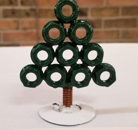 If you are needing a little desk tree to brighten the spirit at the office, we have a tree made from exhaust flange nuts, and a bit of a bolt as the trunk! Painted in evergreen, with a brown trunk, and the base painted in snow white. Clear coated for long lasting protection. There are a few of these made, and they all vary just a little bit in height but all the same materials. Dimensions: 3-3.5in tall , 2.75in wide. The base in 1.5in wide. Weighs less than 1/2 pound Diy Nuts And Bolts Crafts, Nut And Bolt Art, Nuts And Bolts Christmas Ornaments, Nuts And Bolts Art, Metal Christmas Decor, Metal Christmas Ornaments, Metal Crafts Diy, Metal Flower Nuts And Bolts, Nuts And Bolts Keychain