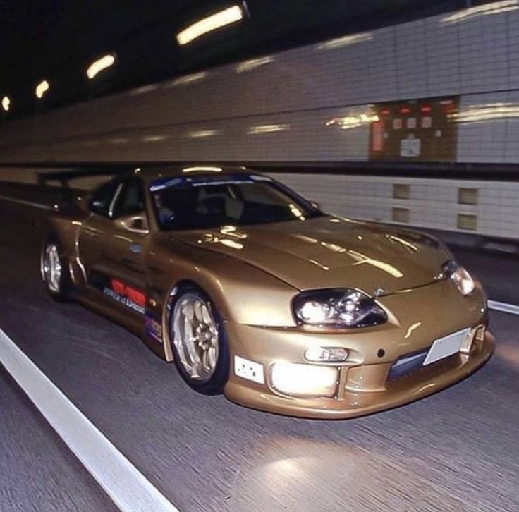 a gold colored sports car driving down the road at high speed with its hood up