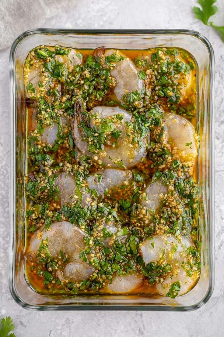 a glass casserole dish filled with meat and vegetables, garnished with herbs