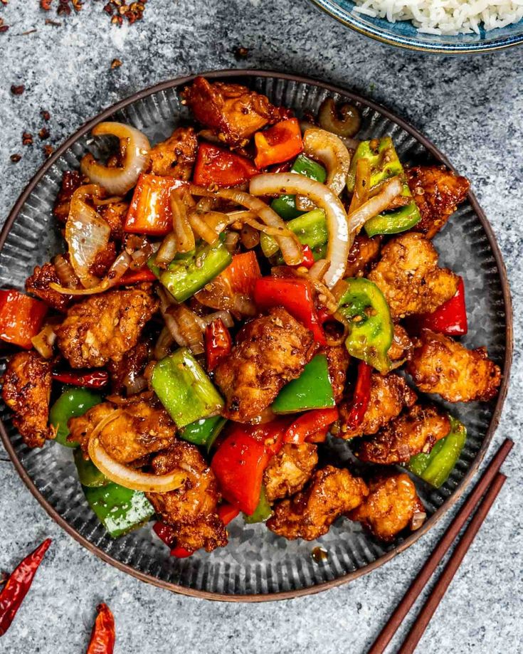 a plate full of chicken and vegetables with chopsticks next to it on a table