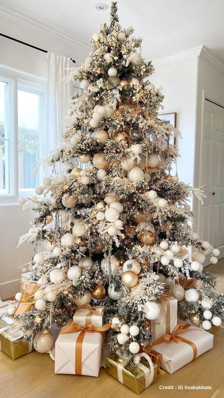 a white christmas tree with gold and silver ornaments on it's branches is surrounded by presents