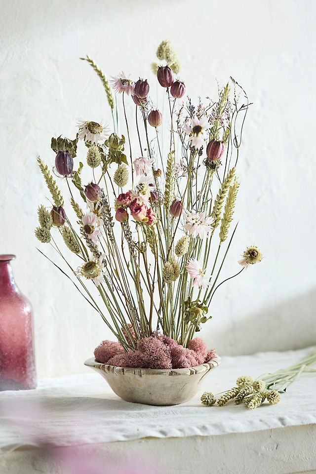 a white bowl filled with lots of flowers on top of a table next to a pink vase