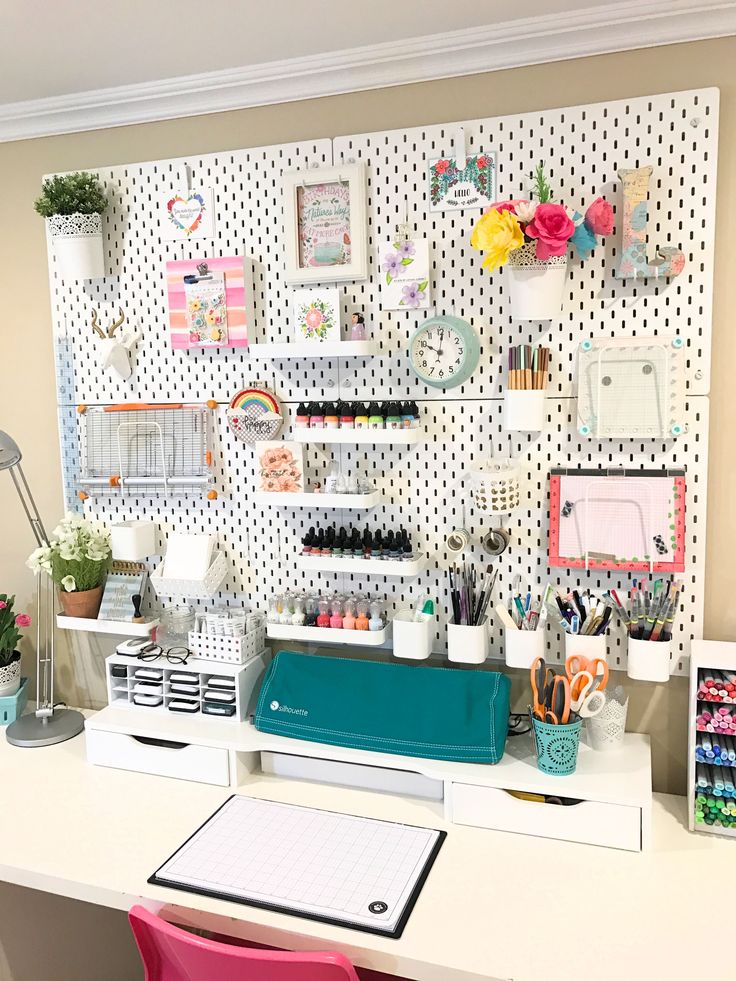 an office desk with lots of clutter on the wall behind it and a pink chair next to it