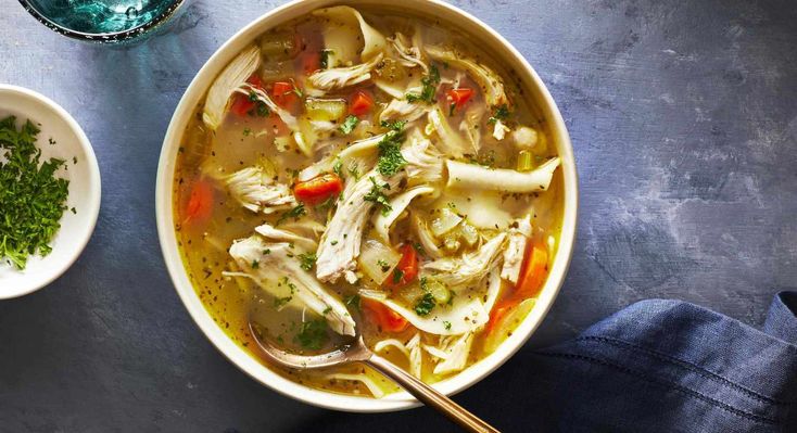 a bowl filled with chicken noodle soup next to two bowls of vegetables and herbs