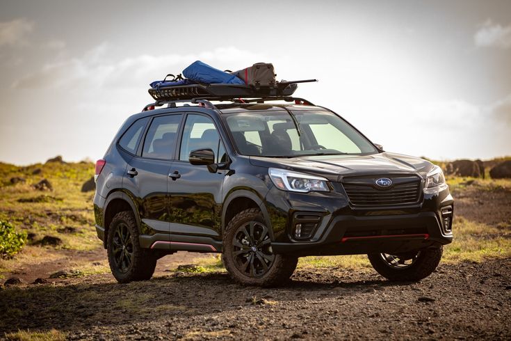 a black subarunt parked on the side of a dirt road with luggage strapped to it's roof