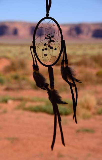 a dream catcher hanging in the desert with mountains in the backgrouds behind it