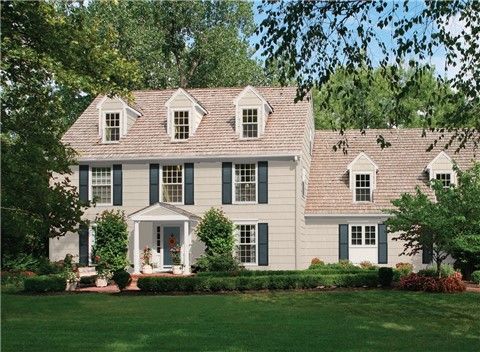 a yellow house with green shutters on the front and side windows, surrounded by trees