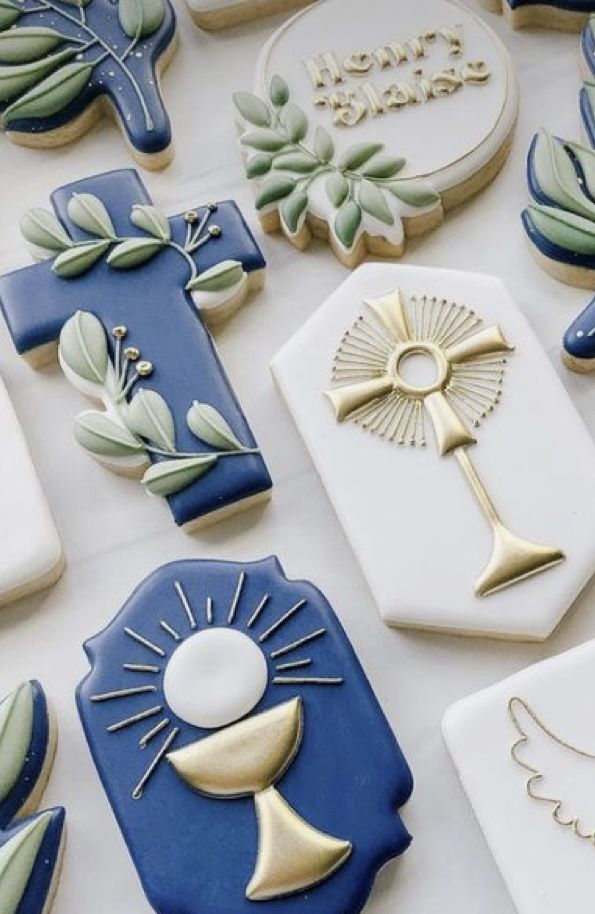 many decorated cookies are on a table with white and blue icing, one has a gold cross