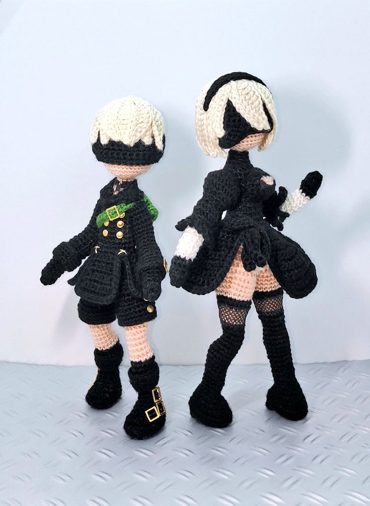 two crocheted dolls are dressed in black and white outfits, one is holding a doll's hand