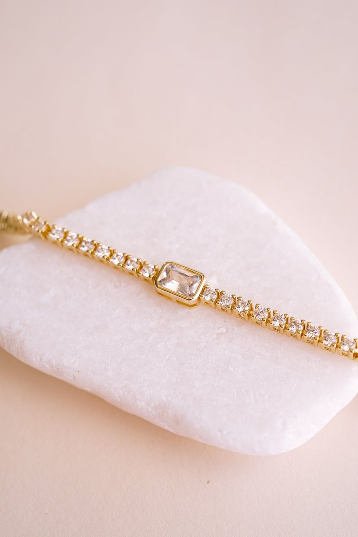 Meet your new favorite accessory: the Amelia Brilliant Cut Tennis Bracelet! We love how it effortlessly adds sparkle to your everyday look, whether you're dressing up for a date night or just want to feel a bit more glam. With its row of dazzling stones and eye-catching emerald cut center, all set in delicate 14k gold plating, this bracelet makes every outfit feel a little more special. The perfect blend of chic and sophisticated, the Amelia Bracelet lets you shine in your own unique way.BRACELE Gold Arm Band, Dainty Gold Bracelet, Armband Gold, Bracelet Tennis, Bridal Jewelry Collection, Gold Armband, Wedding Jewelry Bracelets, Bridesmaid Bracelet, Bridal Bracelet