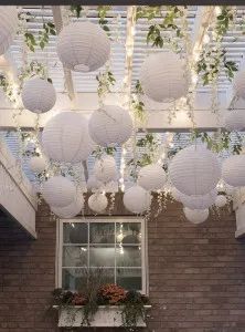 white paper lanterns hanging from the ceiling above a window with potted plants on it