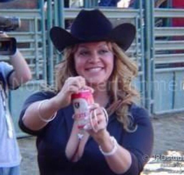 a woman wearing a cowboy hat and holding a bottle in front of some people at a rodeo