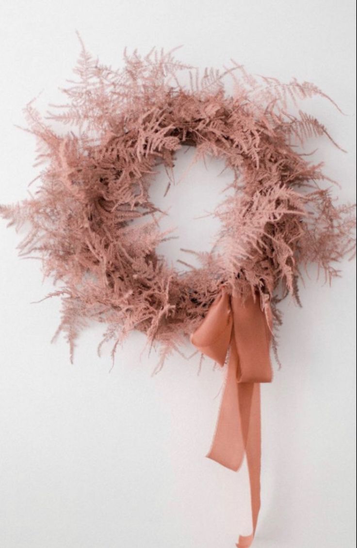 a pink wreath with an orange ribbon hanging from it's side on a white wall