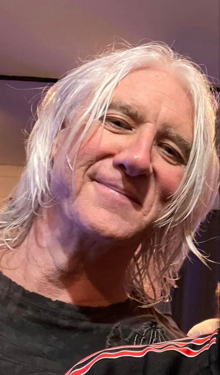 an older man with long white hair and a black shirt is smiling at the camera