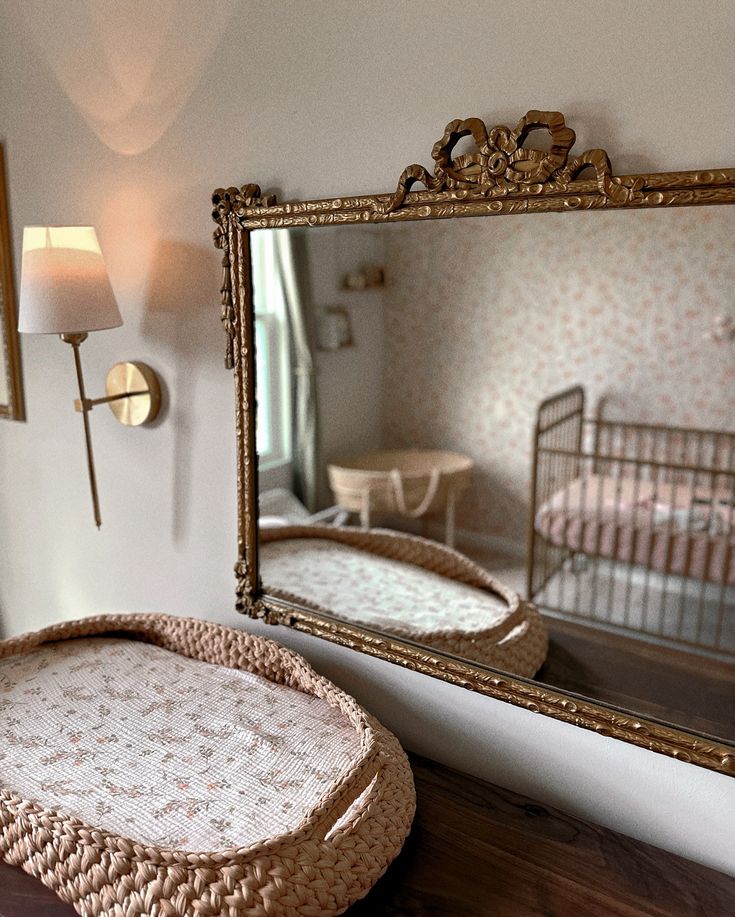 a mirror sitting on top of a wooden table next to a baby crib and lamp