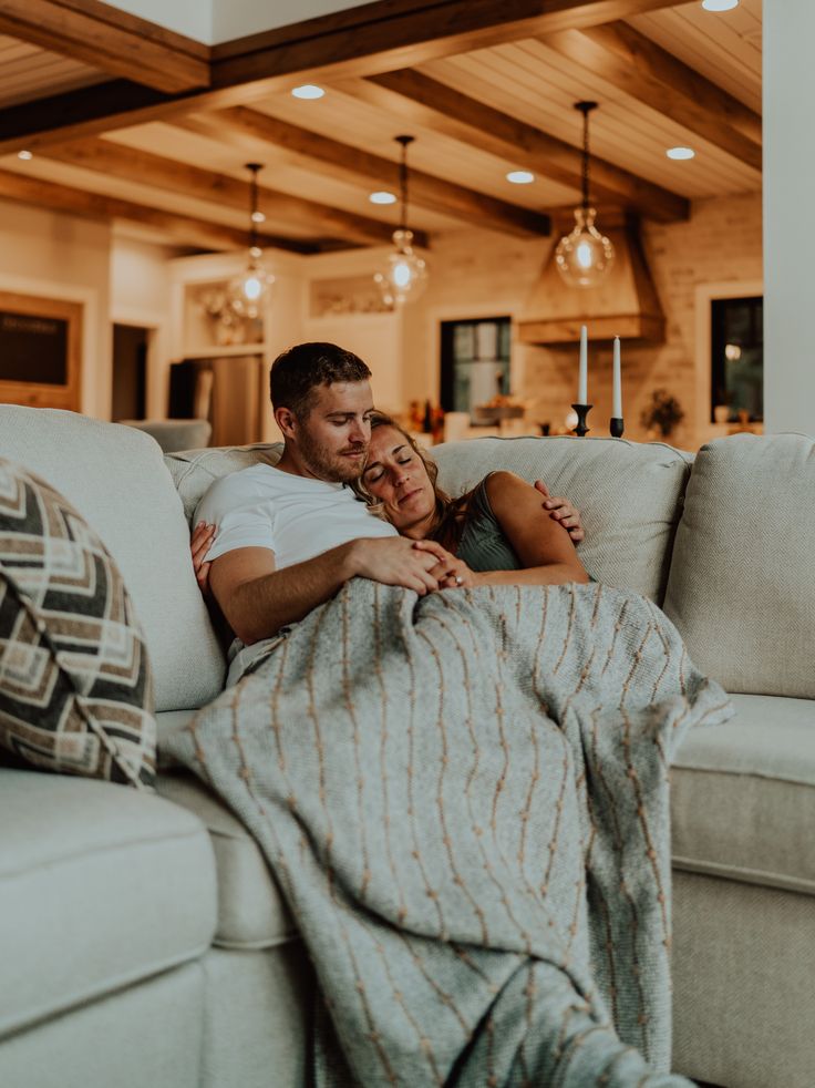 a man and woman cuddle on a couch under a blanket in the living room