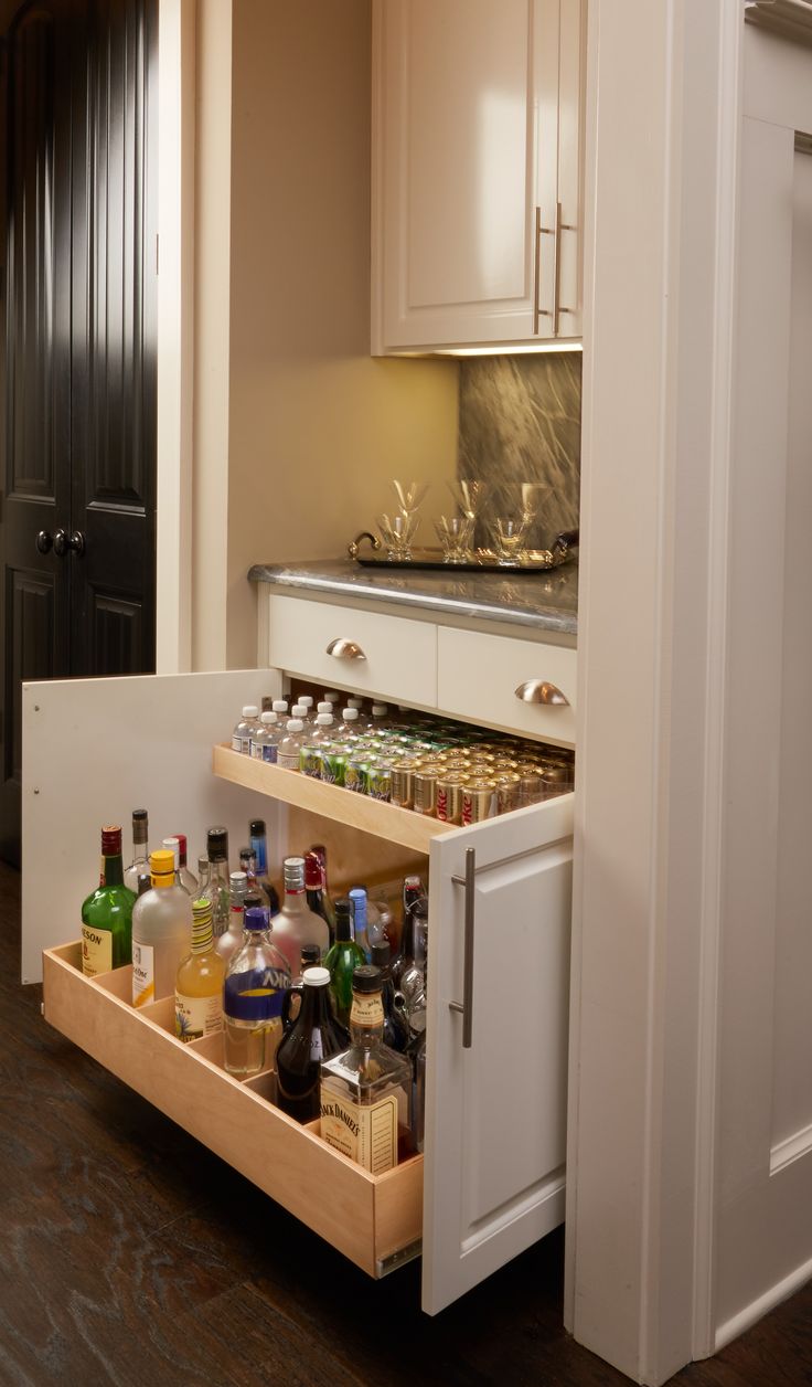 an open drawer in the middle of a kitchen with bottles and glasses on top of it