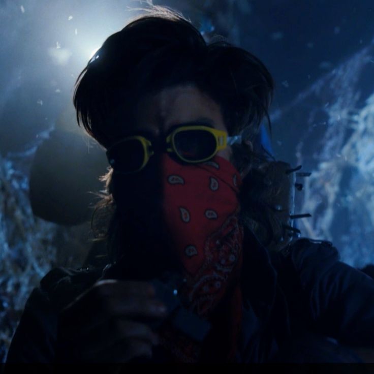 a man with sunglasses and a red bandana covering his face in front of a rock wall