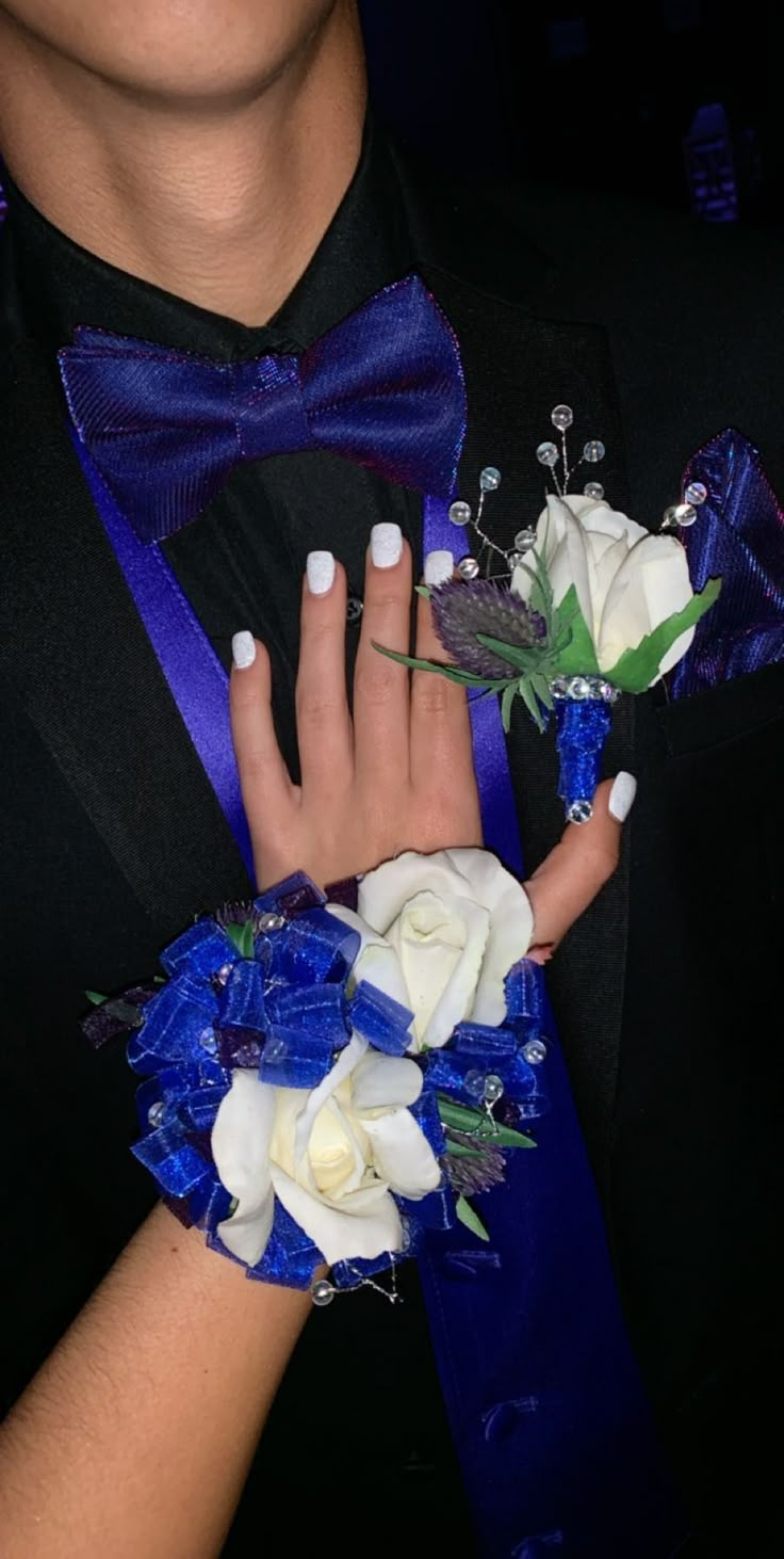 a man in a tuxedo holding two white and blue flowers with his hands