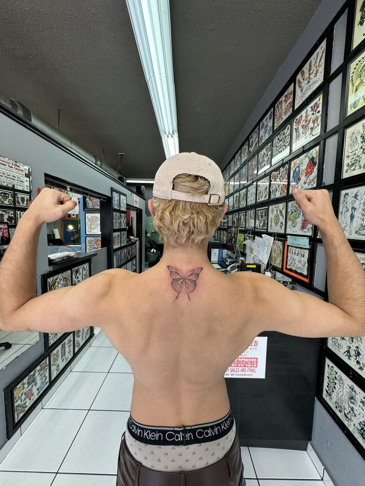 a man with a bow tattoo on his back in front of a wall full of pictures