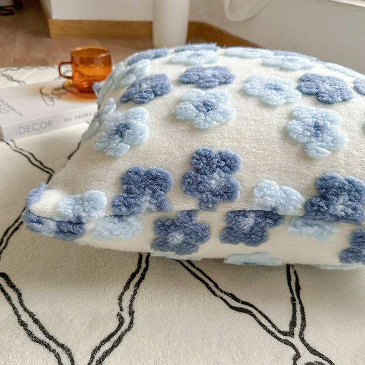 a white and blue pillow sitting on top of a rug next to a glass cup