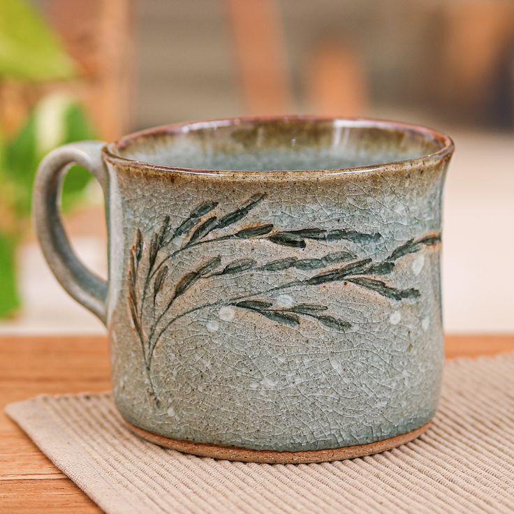 a coffee cup with some plants painted on the inside and outside, sitting on top of a place mat