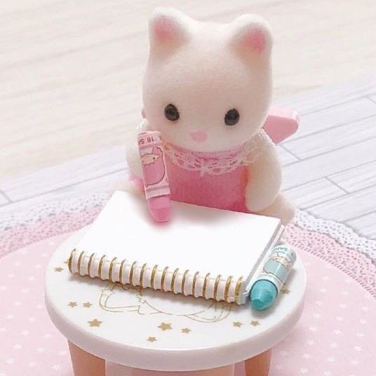 a small toy cat sitting on top of a table next to a notebook and pen