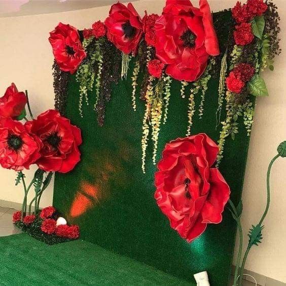 red flowers and greenery are displayed on a green backdrop in the corner of a room