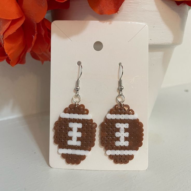 a pair of brown and white beaded earrings with a football on the side, hanging from a card board