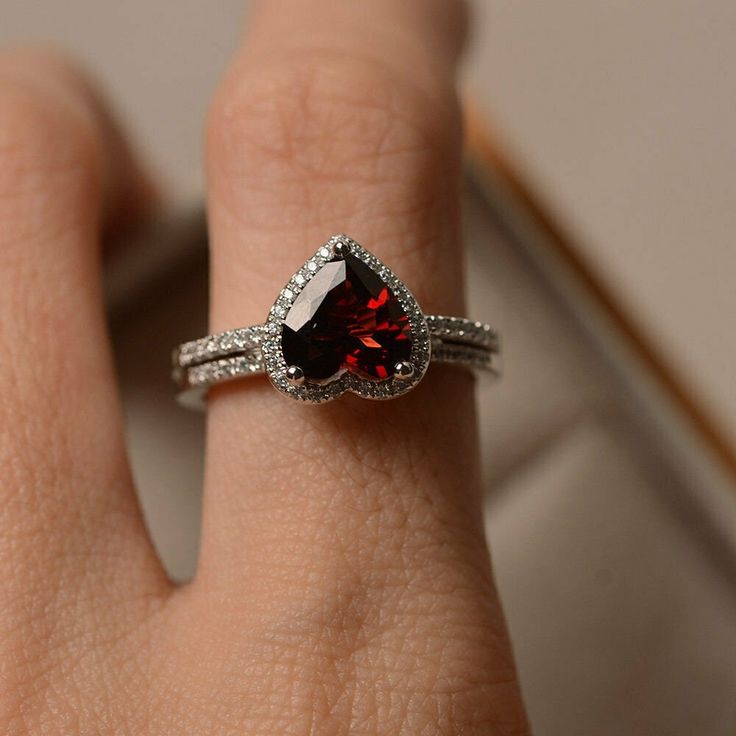 a close up of a person's hand wearing a ring with a red stone