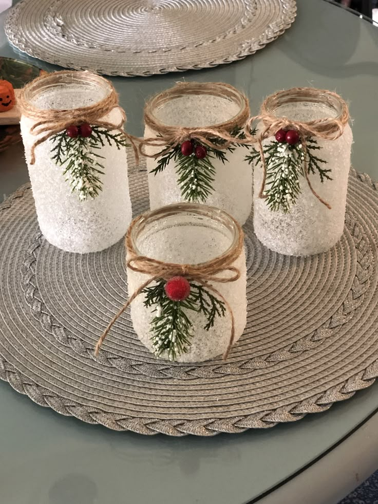 four mason jars decorated with evergreen and red berries are sitting on a placemat, tied with twine