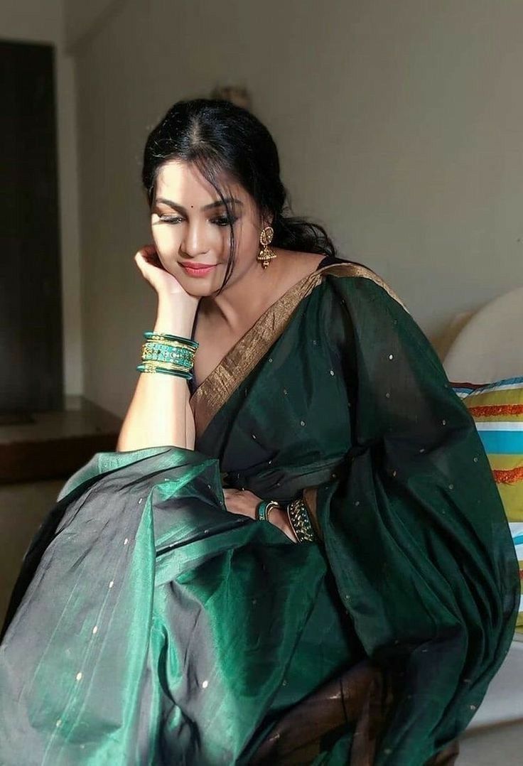 a woman sitting on top of a bed wearing a green sari and holding her hand to her face