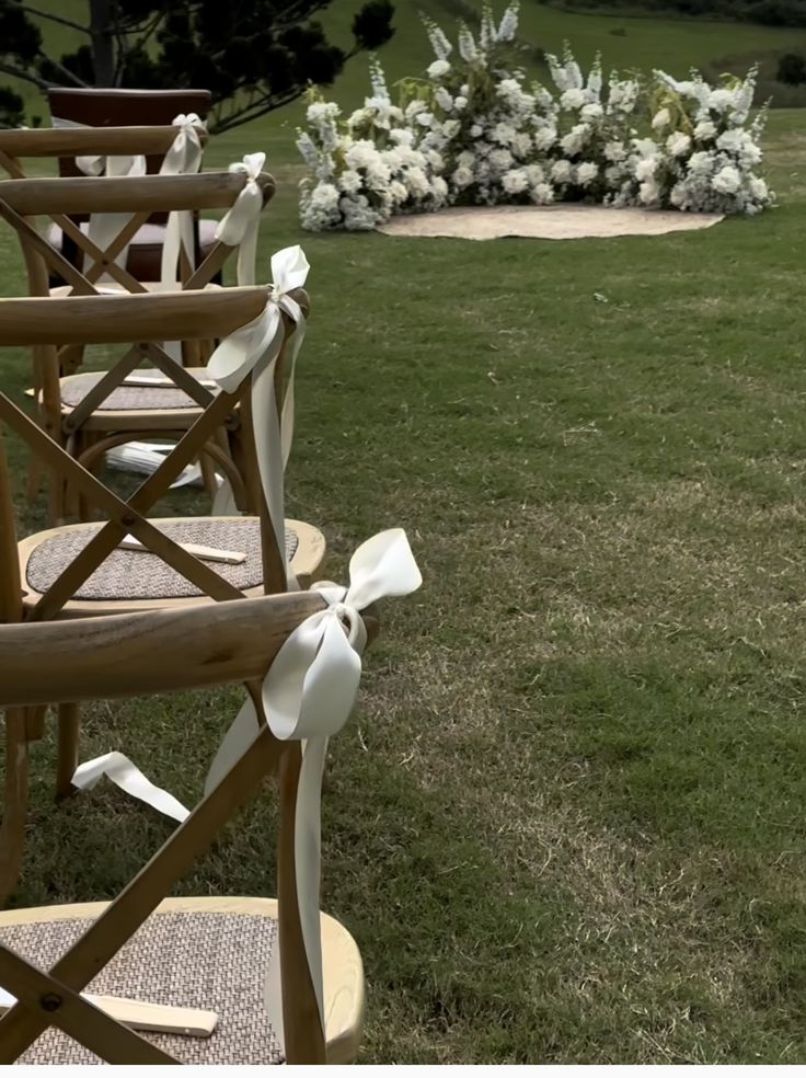 rows of wooden chairs sitting on top of a lush green field next to a white flower arrangement