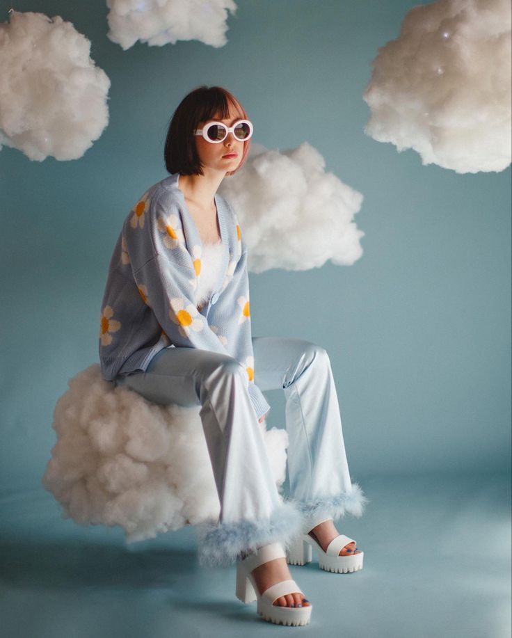 a woman sitting on top of a cloud wearing sunglasses