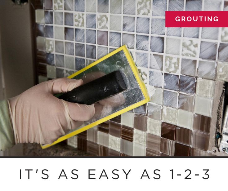 a person using a sponge to clean a tile wall with a grouting tool